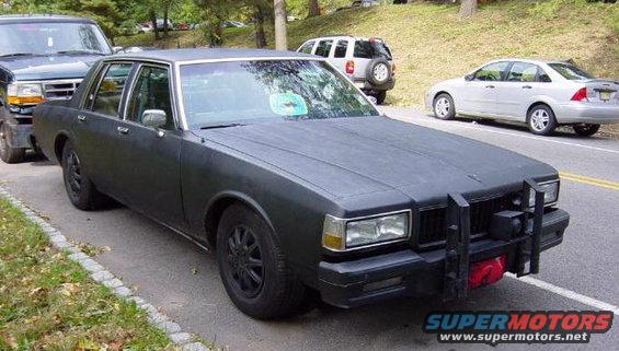 matte black sedan with push bar parked on side of road, other cars visible