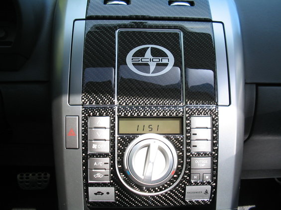 Carbon fiber trim surrounds Scion logo and car interior controls including hazard lights, A/C, and temperature settings
