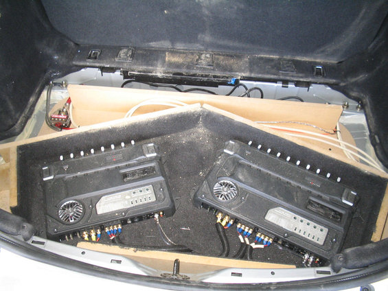Car trunk interior showing two car audio amplifiers installed in a custom enclosure