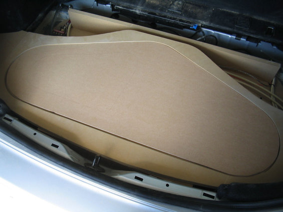 Car trunk interior with large, curved, light brown wood paneling and coiled cables visible