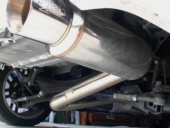 Close-up of a car's rear suspension and exhaust pipe. The exhaust pipe has a brand name visible