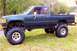 2004 Jeep TJ - Lifted 1984 Toyota pickup truck with oversized tires parked on grass.