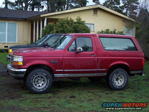 Red Ford Bronco parked next to a black truck in front of a house