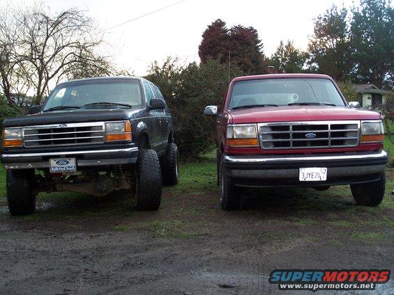 Two Ford trucks, a black SUV and a red pickup, parked front-facing on a dirt lot