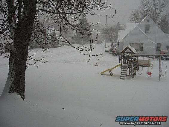 Snowy street with houses and a playground. A tree is in the foreground