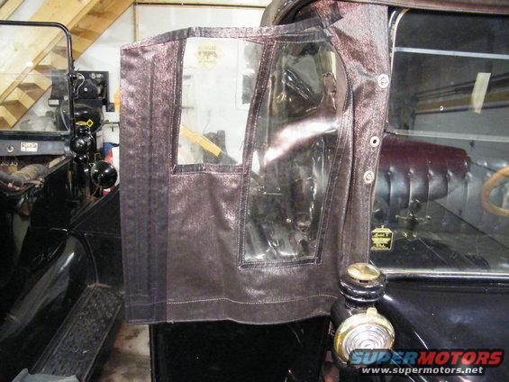 Side view of a vintage car's fabric door with clear windows. A badge is visible on the door