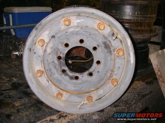 Gray steel wheel rim with 6 lug nuts, showing rust and wear