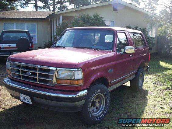 Maroon Ford Bronco parked in front of a house, with a black Ford truck behind it