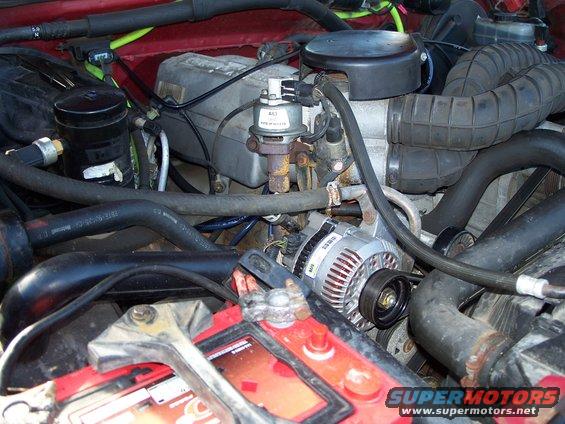 Engine bay with red paint, showing alternator, battery, hoses, and air intake. Some rust visible