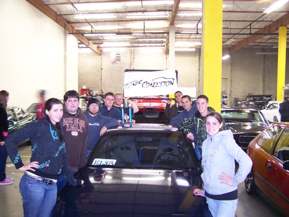 People behind a table with a car in the background