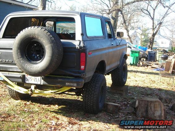 Gray 1978 Ford Bronco with spare tire mounted on rear, lifted suspension, and yellow straps attached to bumper
