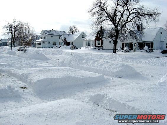 Snowy street with houses and a car barely visible on the left