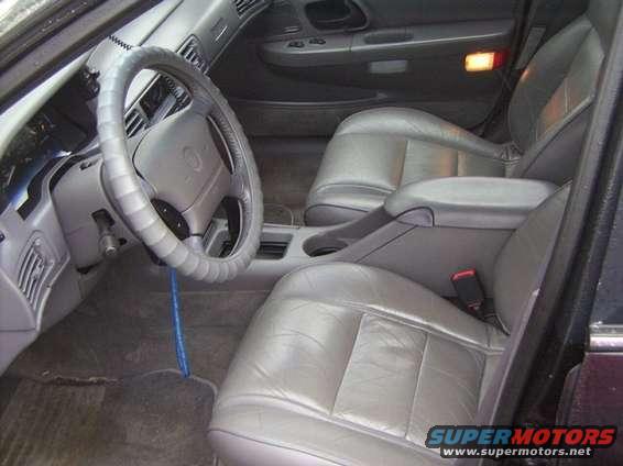Car interior with gray leather seats, steering wheel, and dashboard. A blue cord hangs from the steering column