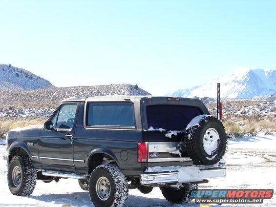 Dark gray 1996 Ford Bronco with a spare tire on the back, parked in the snow with mountains in the background