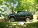 1982 Ford Bronco - A dark green Ford Bronco sits in a grassy yard with its hood open, appearing to be worked on.