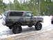 1989 Ford Bronco - A lifted Ford Bronco with camouflage paint sits on a snowy road, with another vehicle partially visible to the right.