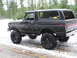 1989 Ford Bronco - This lifted Ford Bronco is parked on a snowy road with trees in the background.