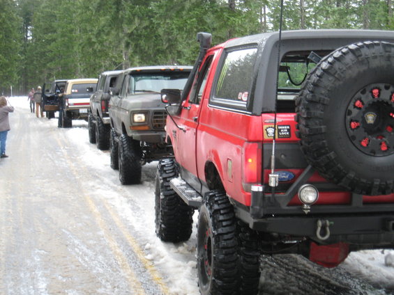 Red Ford Bronco with lifted suspension and large tires, parked on a snowy road