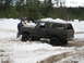 1989 Ford Bronco - A dark brown Ford Bronco is stuck in the snow with two people attempting to free it.
