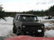 1989 Ford Bronco - A black Ford Bronco navigates a snowy terrain, its large tires kicking up snow.