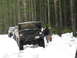 1989 Ford Bronco - A line of off-road vehicles, including a Ford Bronco with its hood up, are parked in a snowy forest.
