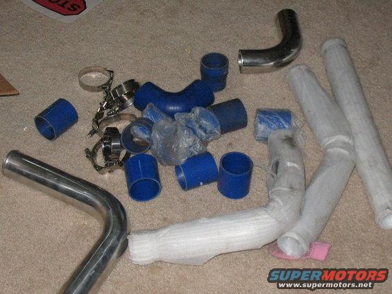 Pile of blue silicone couplers, metal pipes, and hose clamps on carpet