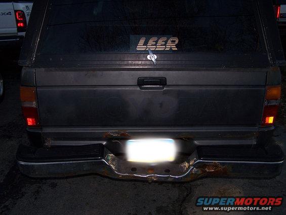 Rear of a pickup truck with a Leer camper shell. Another white truck is partially visible to the left