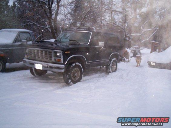 Black 1980s Ford Bronco parked in snow, another vehicle partially visible to the left