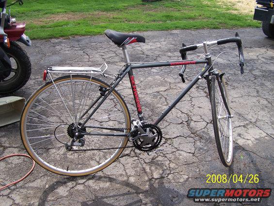 Gray Schwinn bicycle with drop handlebars and a rear rack, parked on cracked asphalt