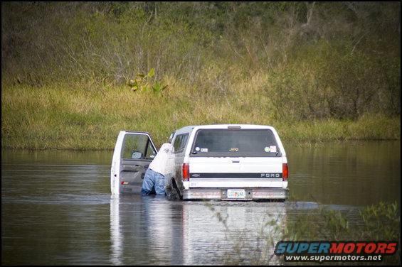 White Ford van with open driver door, partially submerged in water, with person inside