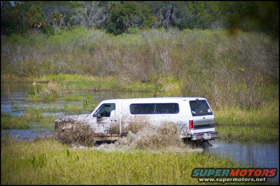 White 1996 Ford Bronco driving through muddy water, splashing