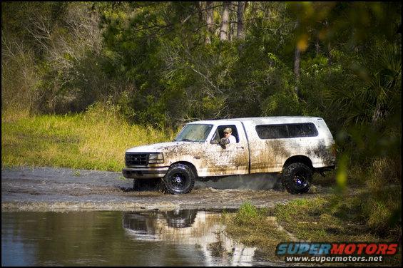 1996 Ford F-150 driving through water, covered in mud. Camper shell on the bed