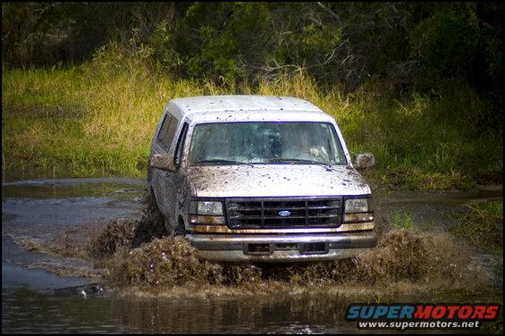 White 1996 Ford F-150 driving through mud and water, front view