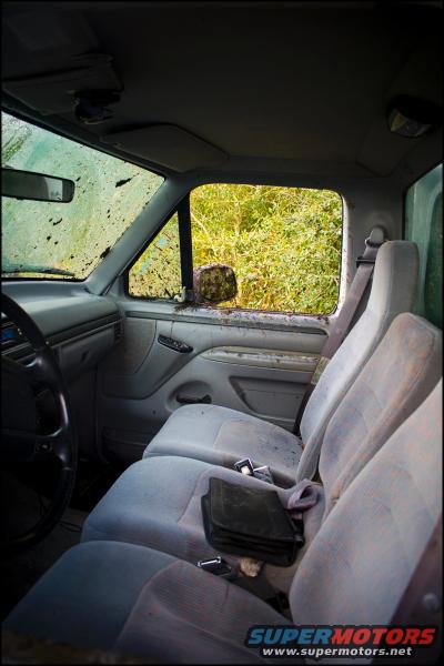 Gray interior of a dirty truck with three seats and a steering wheel. Mud splatters the windshield