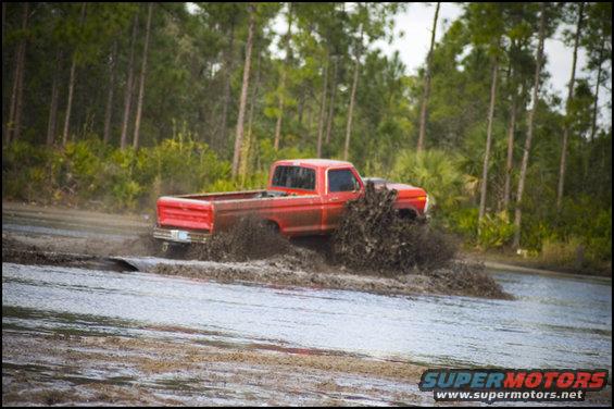 Red 1979 Ford F-150 truck splashing through mud and water