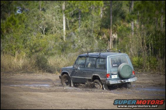 Dark green SUV stuck in mud, rear view. Spare tire on back