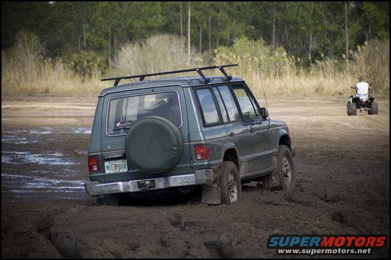 Green SUV stuck in mud with spare tire on back. ATV in background