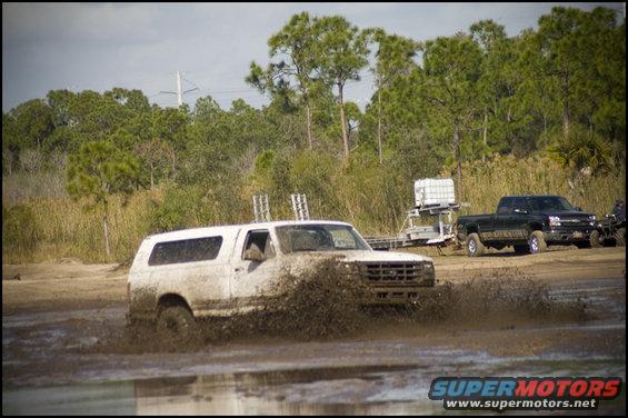 White SUV splashing mud, black pickup truck in background