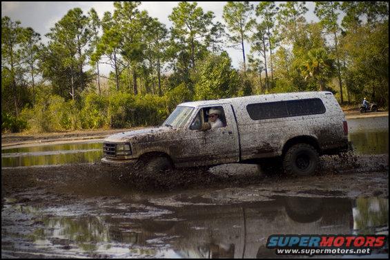 1996 Ford F-150 driving through mud and water, covered in mud. Camper shell on the bed