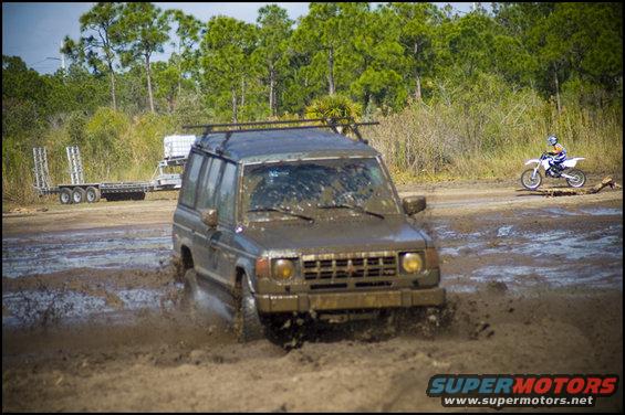 Muddy SUV driving through a puddle with a dirt bike in the background