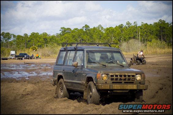Mitsubishi Pajero/Montero stuck in mud, with other vehicles and a person on an ATV in the background