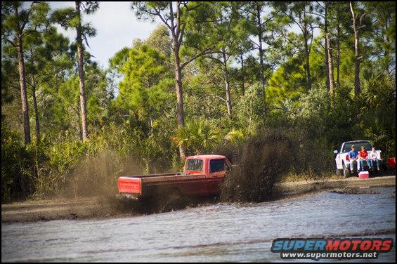 Red 1979 Ford F-150 kicking up mud, white truck parked nearby