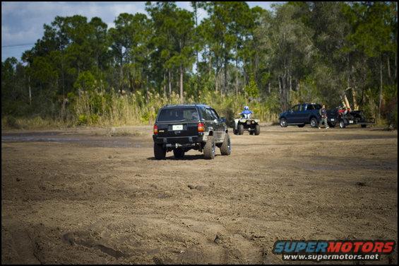 Black SUV, ATV, and trailer with another SUV in background on dirt terrain