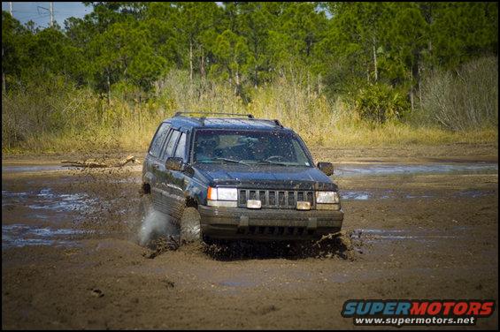 Black Jeep Grand Cherokee splashing mud while driving off-road