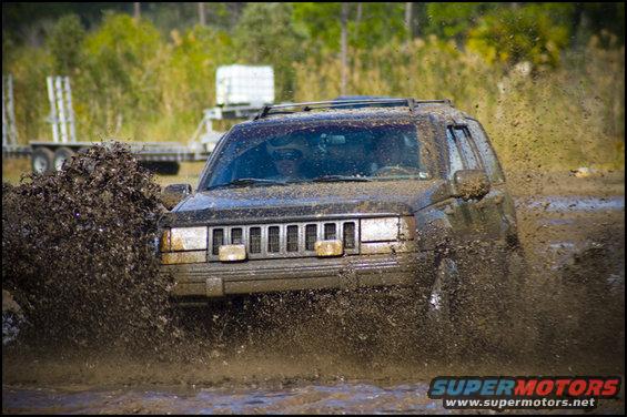 Jeep Grand Cherokee splashing through mud, front view. Trailer in background