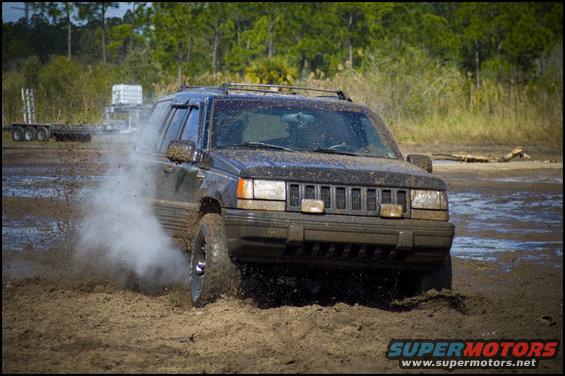 Dark 1996 Jeep Grand Cherokee driving through mud, kicking up spray