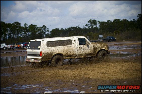 1996 Ford Bronco with camper shell driving through mud, splashing water