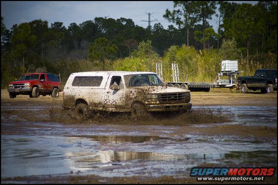 Mud-splattered white SUV driving through a muddy field. Grille indicates 1992 model year