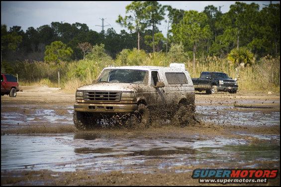 White 1996 Ford Bronco splashing through mud, front 3/4 view
