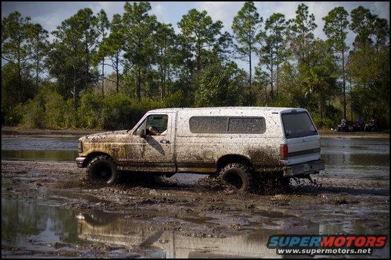 1996 Ford F-150 side view, covered in mud, driving through a muddy field